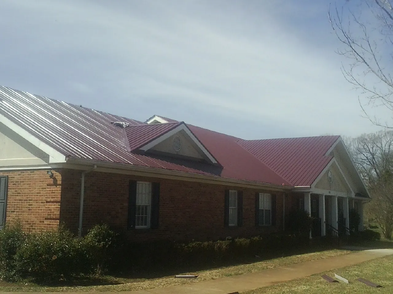 Red metal roof with gabled entries on a long brick building, from a Hail Damage Roof Repair job in Unionville